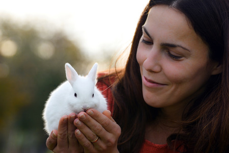 The smiling woman is holding a little cute white bunny.の写真素材