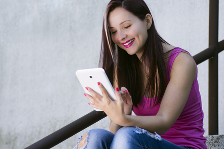 Beautiful smiling young woman with white tablet outdoors.の写真素材