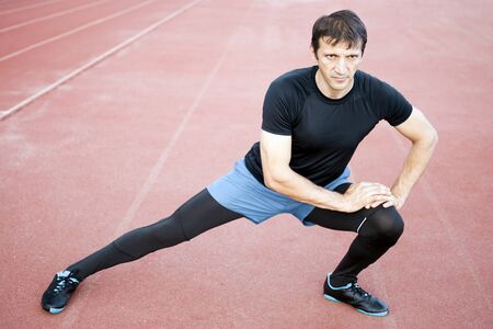The athlete in sportswear is exercising his legs outdoors.