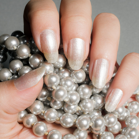 Female hand with glossy white nails holds pearls.の写真素材