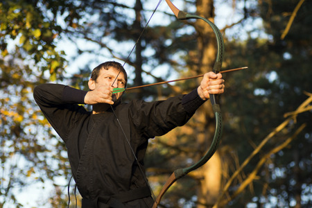 The archer in black kimono takes aim with bow and arrow in nature.