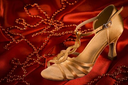 Golden latin dance shoe is on red satin background with red pearls.の写真素材