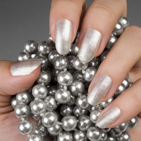 Female hand with glossy silver nails is holding pearls.の写真素材