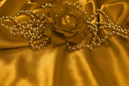 Golden rose and gold pearls as decoration are on golden satin.の写真素材