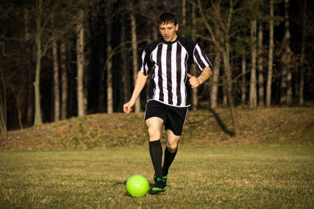 The football player is playing football outdoors in the park.