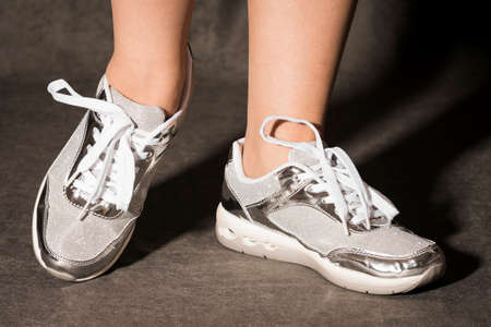 Female legs in silver fashionable sport shoes on gray background.の写真素材