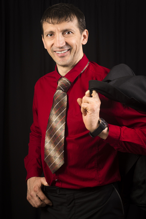 Elegant handsome smiling man is posing in red shirt and necktie on black background.の写真素材