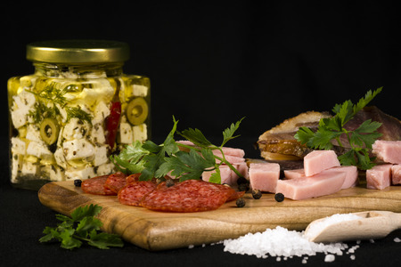 Appetizer, different meat products and feta cheese are on cutting board on black background.の写真素材