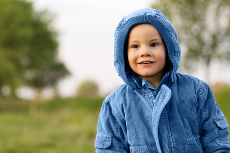 Little child is in blue jacket and hood outdoors in nature.の写真素材