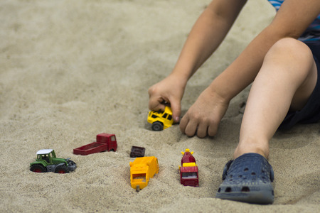 Little boy is playing with toy cars in the sand.の写真素材
