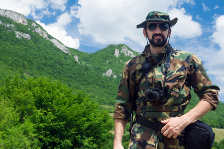 The soldier in uniform with camera is outdoors in nature with mountains on background.の写真素材