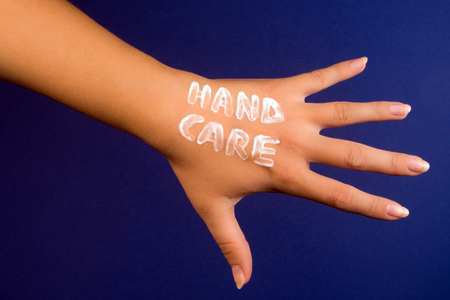 Female hand with hand cream hand care text on blue background, hand and skin care concept.の写真素材