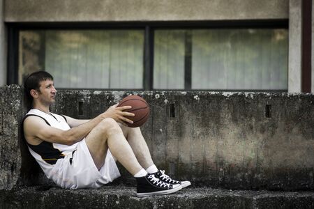 The basketball player is resting outdoors on the concrete.