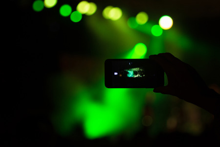 Silhouette of hand with mobile phone or camera on green concert lights background.