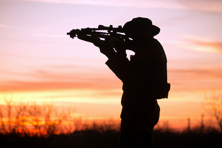 The soldier or hunter is aiming with cross-bow at sunset in nature, silhouette.