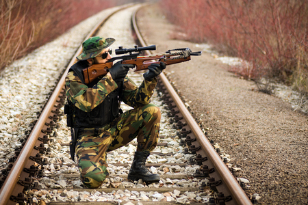 The soldier or hunter in military uniform is aiming with cross-bow on railway outdoors in nature.の写真素材