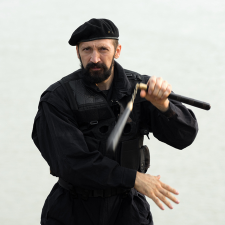 The security man in black uniform and beret is practicing martial arts with nunchaku on white...