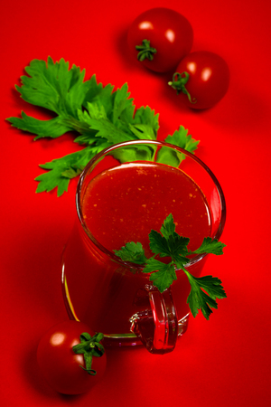 The fresh cherry tomato juice with parsley and celery is on red background.の写真素材