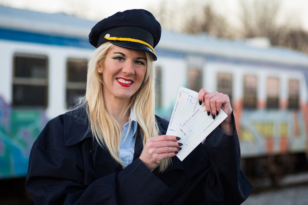 The smiling female railway worker or railroad employee is showing the tickets outdoors on railway station.の写真素材