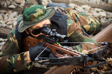 The military man is aiming with crossbow weapon and lying down on railway track.の写真素材