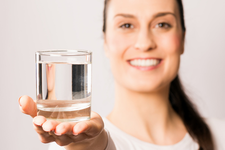 Pretty smiling woman is holding in hand a drinking glass with water, water drinking for health, healthy lifestyle.の写真素材