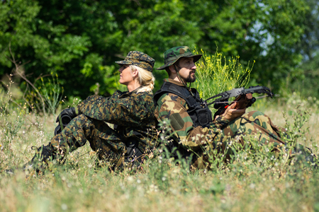 The female and male soldiers in different military uniforms are sitting down in grass in nature.の写真素材