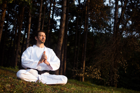 Man in white kimono is practicing meditation in nature in forest.の写真素材