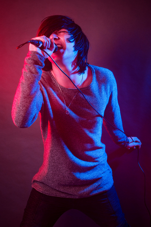 The teenage boy or young singer guy is singing and screaming in microphone on the stage.の写真素材