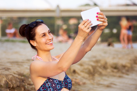 Attractive smiling woman in bikini is using tablet on the beach.の写真素材