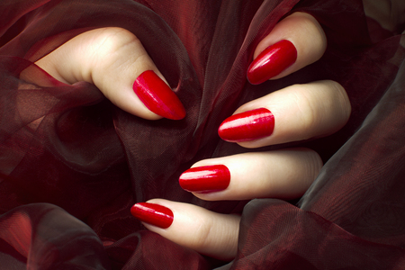Female hand with sensual red nails on dark red background, manicure and nail care concept.の写真素材