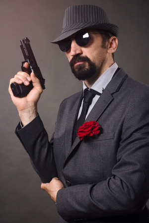 The old-fashioned elegant man in suit, hat and sunglasses is holding a pistol in hand.の写真素材