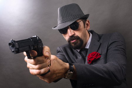 The gangster in elegant suit and hat in vintage style is aiming with pistol.の写真素材