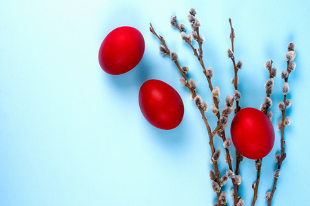 Simple decoration for Easter from three red eggs and willow branches on bright blue background.の写真素材