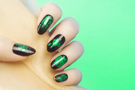 Female hand with green black nails on green background, manicure concept.の写真素材