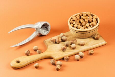 Fresh ripe whole hazelnuts on cutting board and in wooden bowl with nut-cracker on orange...