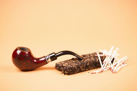 Tobacco pipe or smoking pipe, tobacco and matches on orange background, tobacco products concept.の写真素材