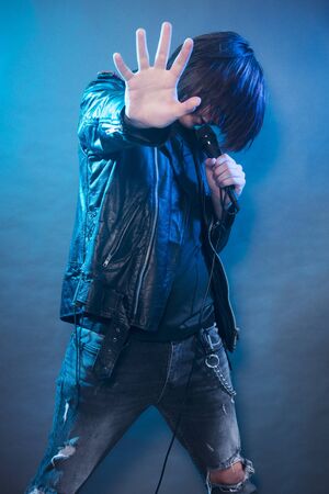 The young guy in black leather jacket is singing rock music and performing on the stage.の写真素材