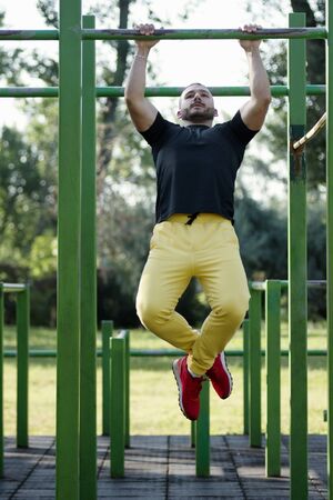The young athlete is doing pullups street workout training outdoors in the park.