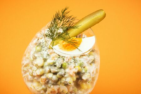 Decorated Russian salad with egg, pickle and dill is in drinking glass on orange background.の写真素材