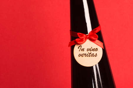 In vino veritas text on wood with red bow on dark wine bottle on red background.の写真素材