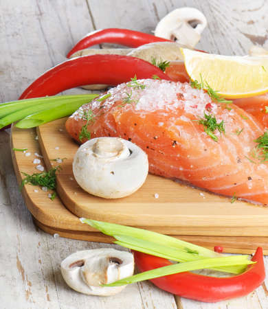 Fresh salmon steak with spices and vegetables on a wooden tableの写真素材