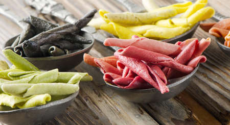 Italian pasta - uncooked multicolored macaroni on a wooden tableの写真素材