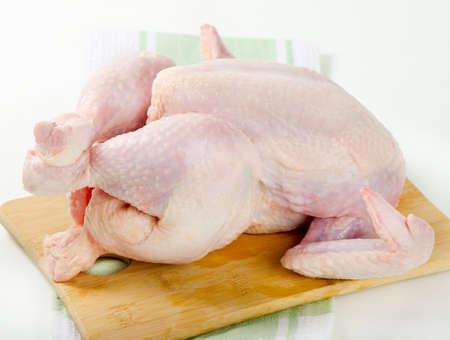 Whole raw chicken on wooden platterの写真素材
