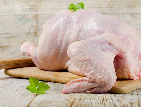 Whole raw chicken with fresh herbs on a wooden tableの写真素材