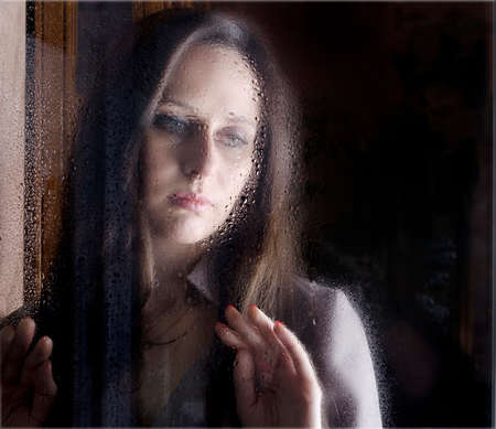 Sad  woman looking through the window with rain dropsの写真素材