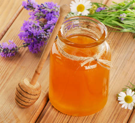 Glass jar of honey with wooden stick and flowers. Selective focusの写真素材