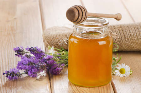 Glass jar of honey with wooden stick and flowers. Selective focusの写真素材