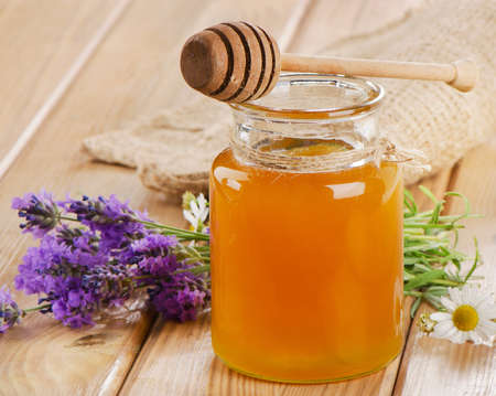 Glass jar of honey with wooden stick and flowers. Selective focusの写真素材