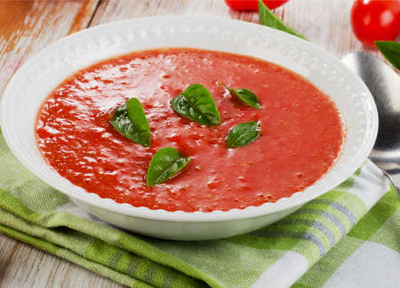 Fresh tomato soup in a white bowl on a wooden tableの写真素材