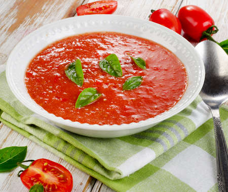 Fresh tomato soup in a white bowl on a wooden tableの写真素材